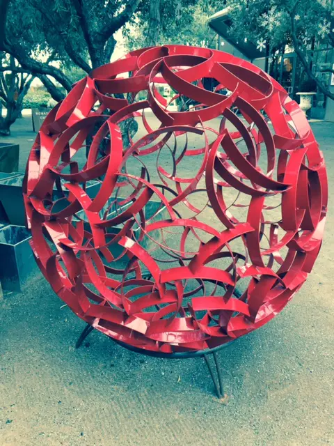 red metal sphere outdoors with trees